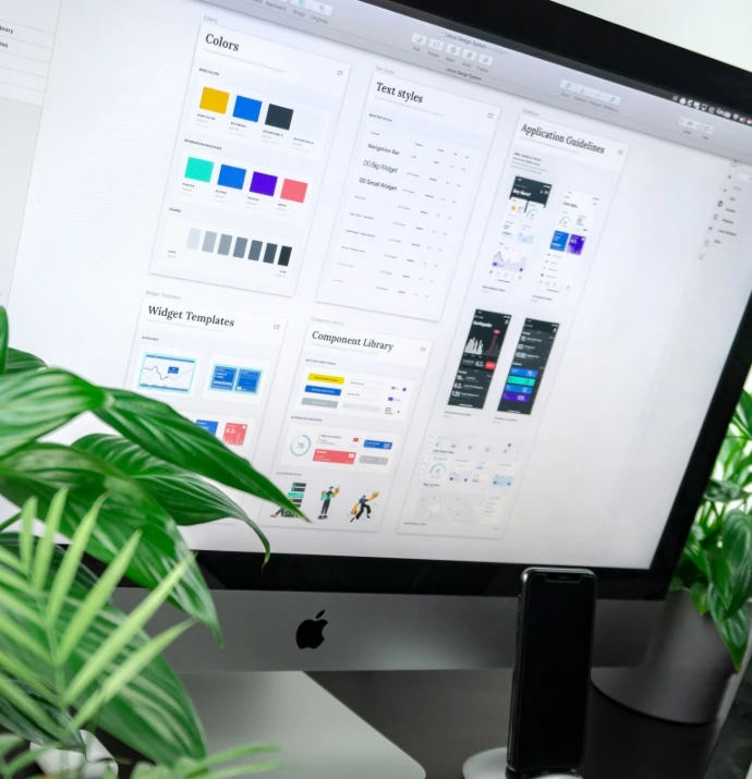 A computer monitor displaying a design system interface with plants on a desk